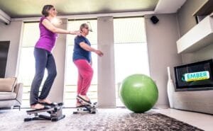 Senior woman exercising at home with personal trainer assisting her with balance and stretching exercises