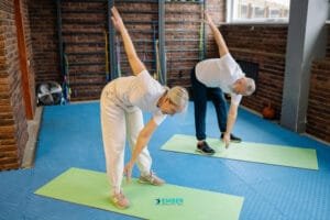 Older man and woman performing a standing cross-body stretch on mats to improve posture and flexibility